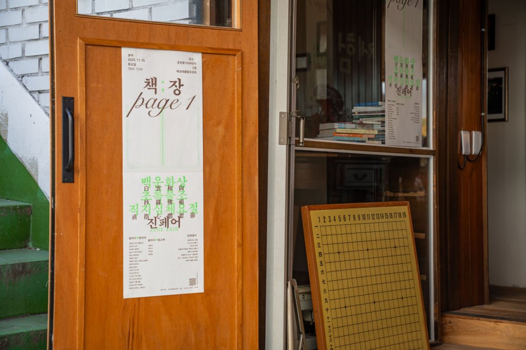 나무 문에 붙은 책;장 page 1 포스터와 문 옆에 세워둔 바둑판