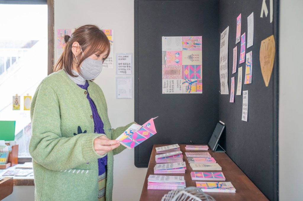 리소천사의 리소 전시 앞에서 분홍색 인쇄물을 펼쳐 보는 관람객
