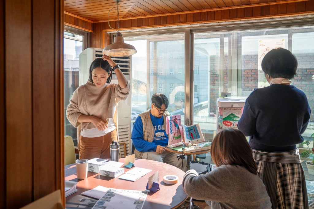 햇빛 드는 창가 테이블에 진과 그림책을 펼쳐두고 부스를 준비하는 창작자들